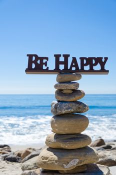 Sign "Be happy" on the top of rocks balancing by Pacific ocean