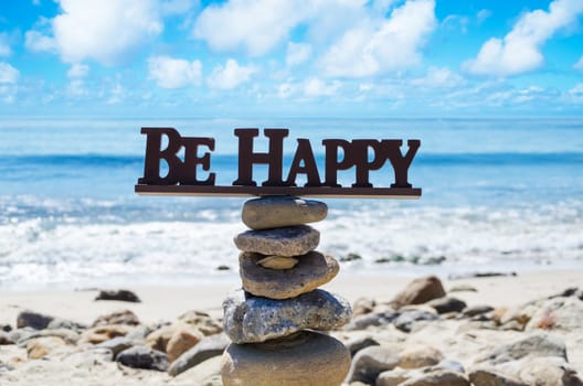 Sign "Be happy" on the top of rocks balancing by Pacific ocean