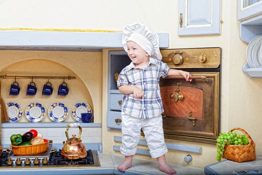 little boy stand on a kitchen table and plays the cook