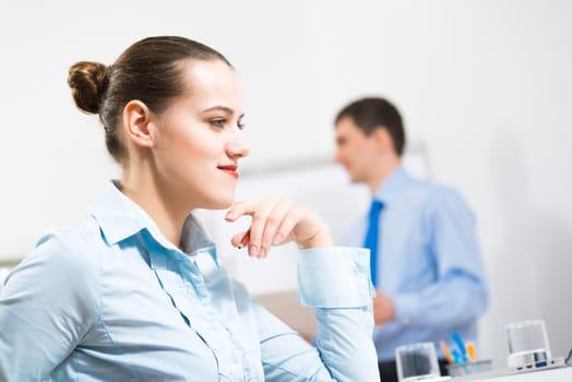 Business woman thinks for a laptop in the office, in the background debating colleagues