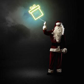 Santa Claus is holding a shining symbol of the gift on a string