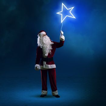 Santa Claus is holding a shining star sign on a string