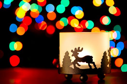 Candlestick with a figure of a deer on the background of blurred lights garlands.