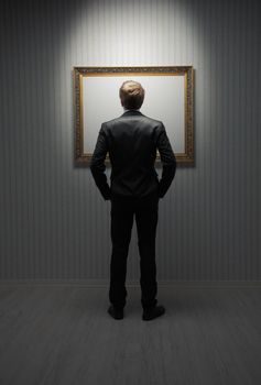A young man standing in front a empty frame in a museum