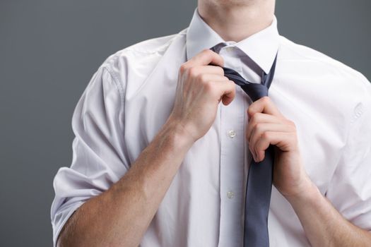 Young business man taking off tie on grey background 