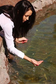 The young beautiful young woman touch fountain hand