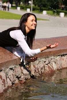 The young beautiful young woman touch fountain hand