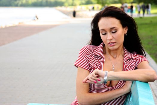 Brunette sitting on a bench and looks at his watch