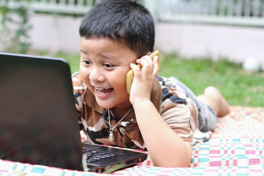 The boys are playing a laptop and talking on the phone. Happily.