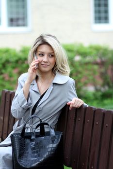 blonde talking on a cell phone while sitting on a bench