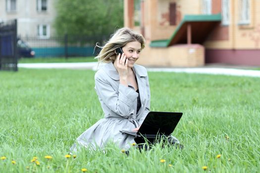 Young blonde girl working on laptop and talking on cell phone