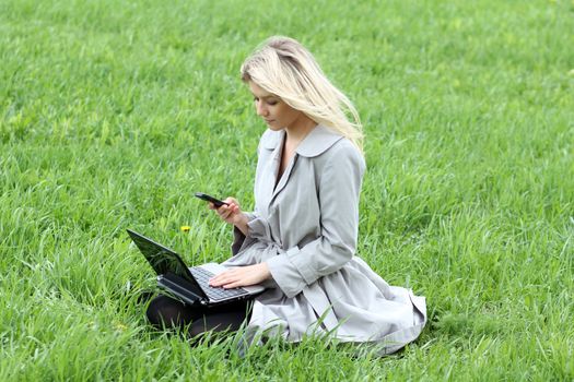 young girl sitting on grass with laptop and phone