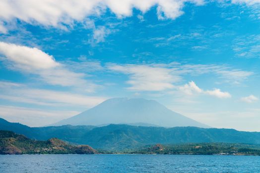 Gunung Agung the highest volcano on Bali island, Indonesia with blue cloudy sky and sea on front.