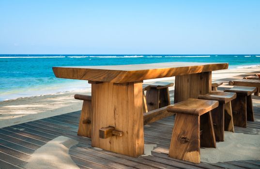 Wooden cafe table and chairs on a tropical beach with blue sea on background