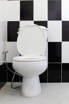 White toilet bowl in the bathroom. Alternating black and white tile backdrop