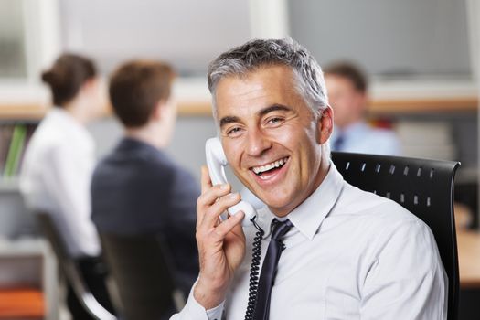 Mature businessman at the phone with colleagues in the background