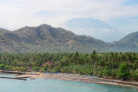 Tropical beach with palms and boats and big volcano on background on Bali in Candidasa, Indonesia