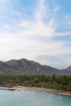 Tropical beach with palms and boats and big volcano on background on Bali in Candidasa, Indonesia