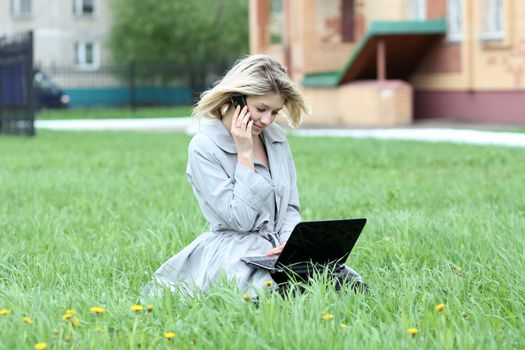 Young blonde girl working on laptop and talking on cell phone