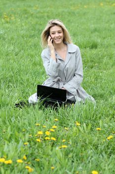 Young blonde girl working on laptop and talking on cell phone