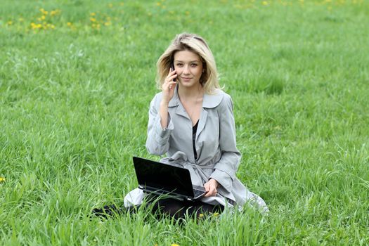 Young blonde girl working on laptop and talking on cell phone