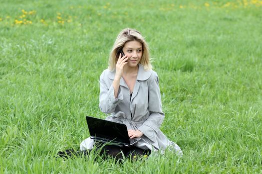 Young blonde girl working on laptop and talking on cell phone