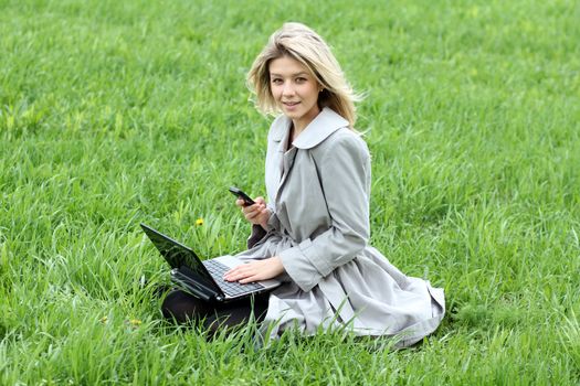 Young blonde girl working on laptop and talking on cell phone