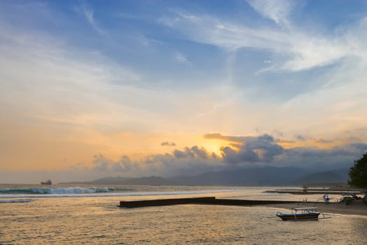 Sunset on a tropical sea shore with breakwaters and boats on Bali in Candidasa, Indonesia