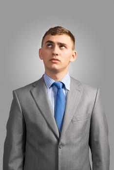 portrait of a young businessman thinking and looking up on gray background