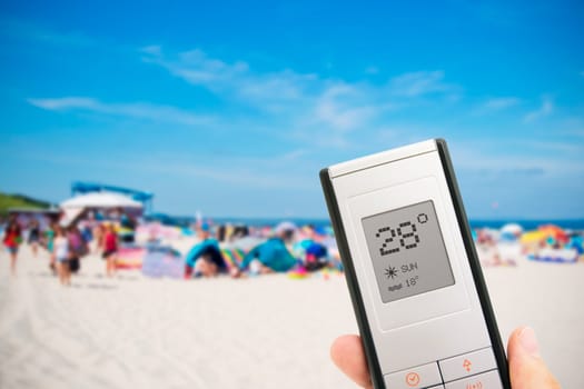 Hand holding electronic thermometer. People on the beach in background