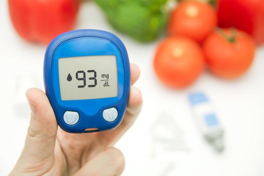 Hand holding meter. Diabetes doing glucose level test. Vegetables in background