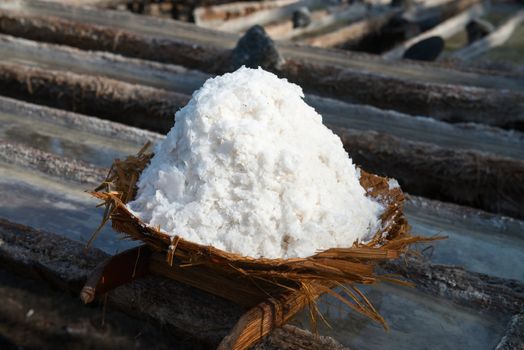 Basket with fresh extracted sea salt on wooden tanks for water evaporation. It is a unique tradition of production dating back over 900 years in Bali, Indonesia.