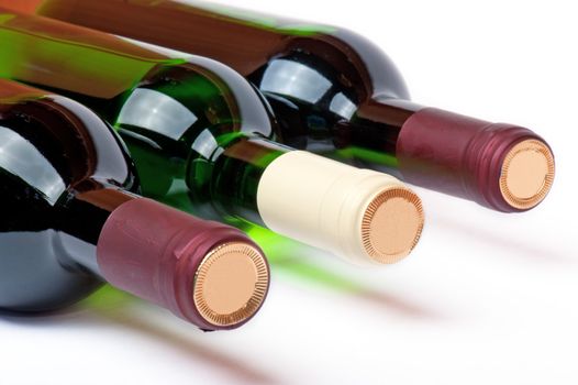 Three bottles with red and white wine lay horizontally on a white background