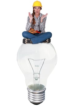 Woman with expression of surprise sat on a big light bulb