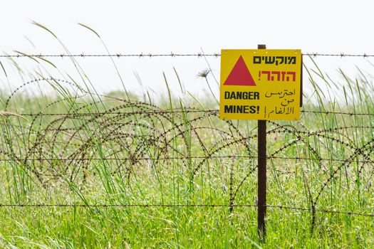 Protective barbed wire fence and warning sign around a minefield on Golan Heights