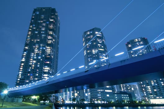 huge residential skyscrapers with illuminated windows beyond illuminated suspension bridge structure in Tokyo, Japan