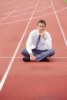 A businessman is sitting on the sports track, conceptual image