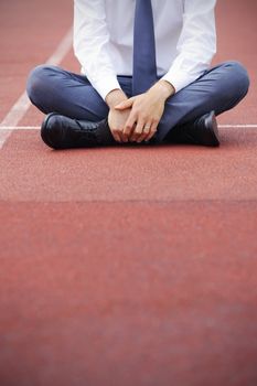 A businessman is sitting on the sports track, conceptual image