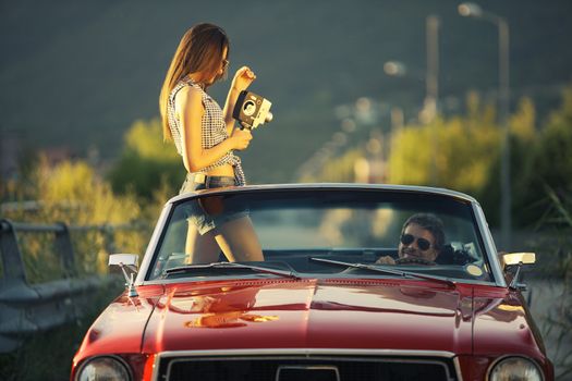 Young beautiful woman filming his boyfriend in a convertible car