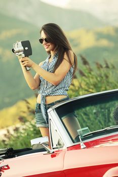 Fashion model with a vintage movie camera in a convertible car