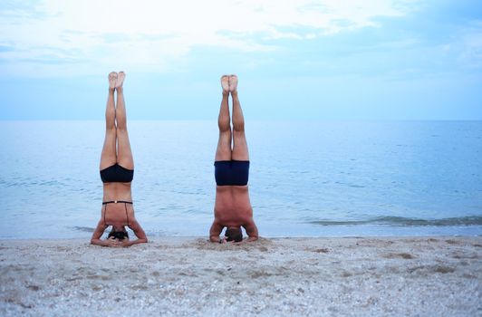 Svelte mature woman and strong man standing on head near sea