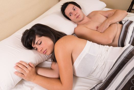 Frustrated guy  in bed looking at his sleeping  partner