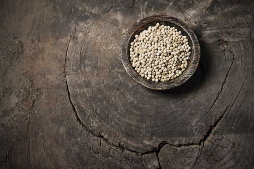 White pepper in grain in a wooden bowl on old wood