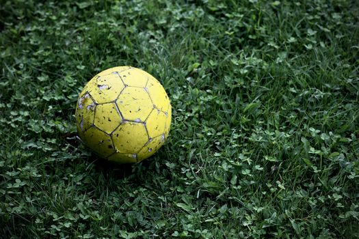 Old yellow soccer ball on green grass