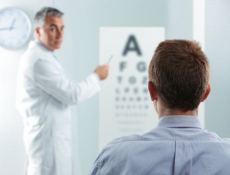 Optometrist and patient, doctor pointing at eye chart 