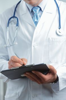 Close up shot of a male doctor writing on clipboard 