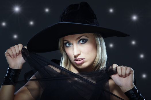 Attractive blond in the Halloween witch costume and hat at night sky background