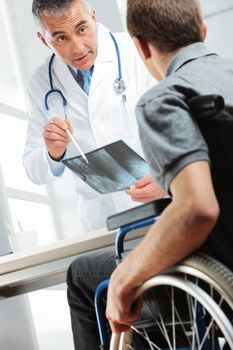 Young man on wheelchair meeting orthopedic doctor. They are looking at x-ray image and consulting about healing.