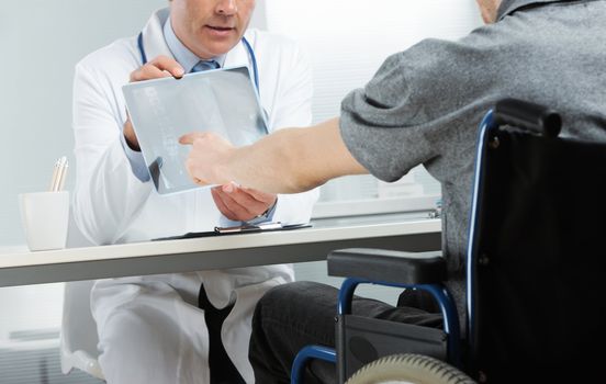Young patient sitting on wheelchair with mature doctor discussing x-ray