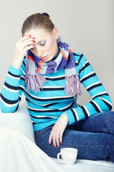 Sick and sorrow woman sitting indoors near the cup with medical drugs